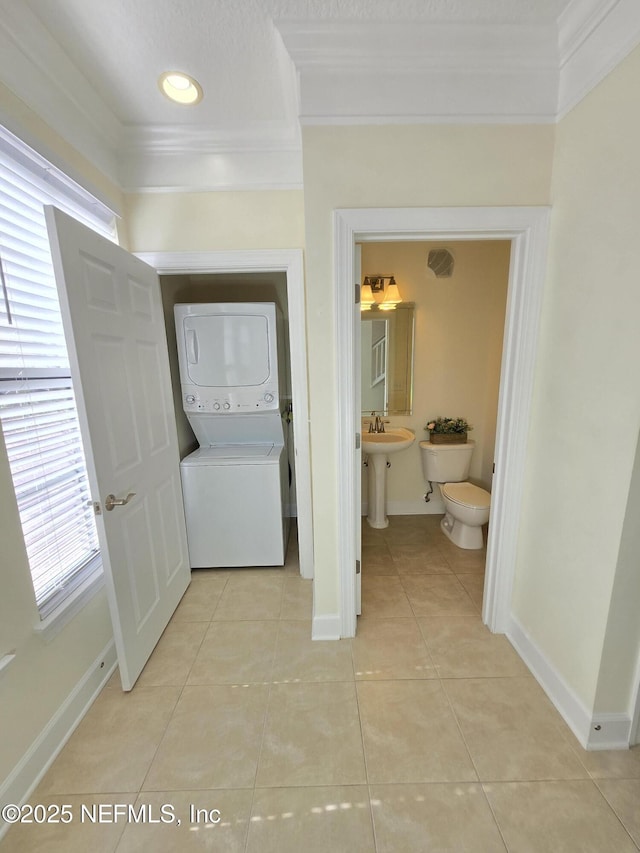 washroom featuring crown molding, laundry area, baseboards, light tile patterned floors, and stacked washer and clothes dryer