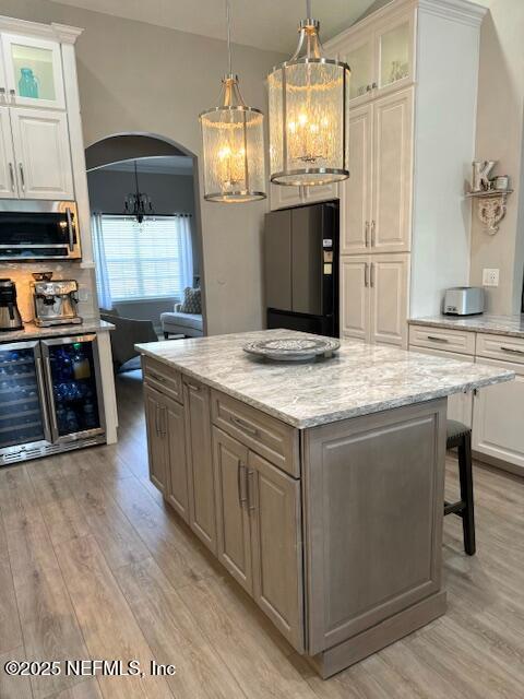 kitchen with freestanding refrigerator, arched walkways, stainless steel microwave, and light wood-type flooring