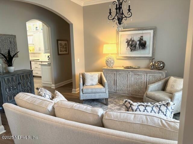 sitting room with arched walkways, wood finished floors, baseboards, an inviting chandelier, and ornamental molding