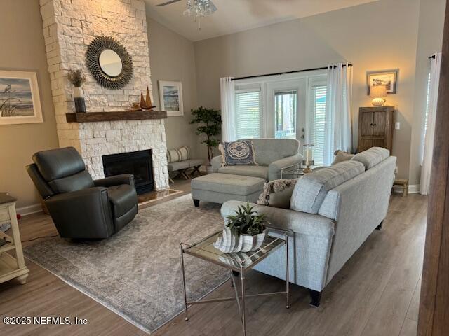 living room featuring high vaulted ceiling, a stone fireplace, a ceiling fan, baseboards, and wood finished floors