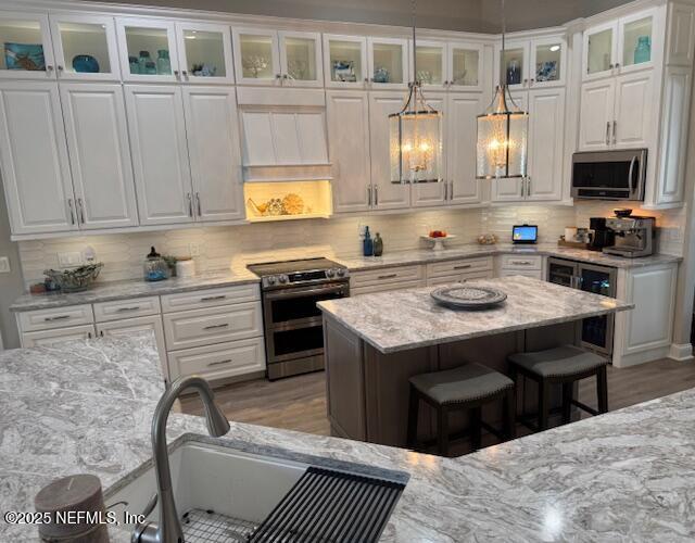 kitchen featuring a kitchen breakfast bar, appliances with stainless steel finishes, light stone countertops, beverage cooler, and white cabinetry