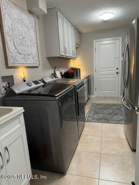washroom featuring light tile patterned floors, laundry area, a textured ceiling, and washer and clothes dryer