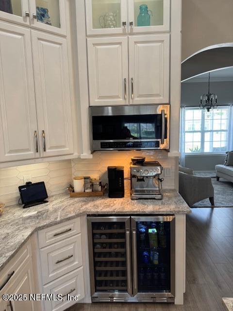 interior space featuring decorative backsplash, wood finished floors, stainless steel microwave, a chandelier, and wine cooler