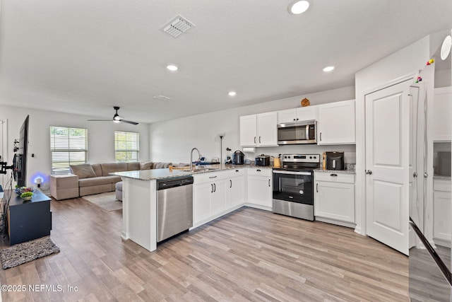 kitchen with visible vents, a peninsula, open floor plan, white cabinets, and stainless steel appliances