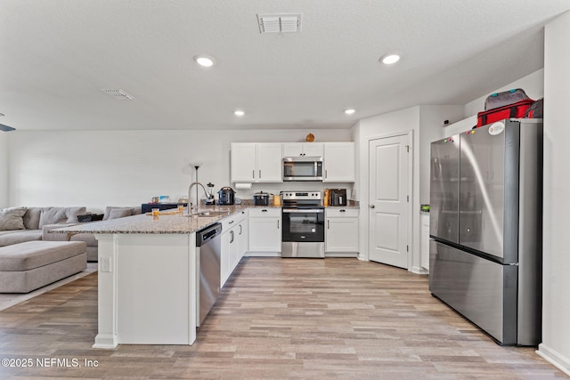 kitchen featuring visible vents, a peninsula, open floor plan, a sink, and appliances with stainless steel finishes