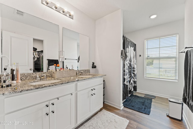full bath with visible vents, a sink, wood finished floors, and double vanity