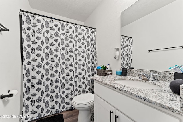 bathroom with a shower with curtain, a textured ceiling, wood finished floors, vanity, and toilet