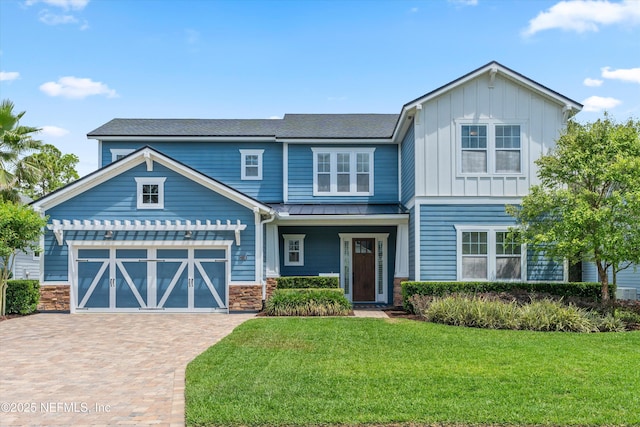 craftsman inspired home featuring board and batten siding, a standing seam roof, a front yard, decorative driveway, and an attached garage
