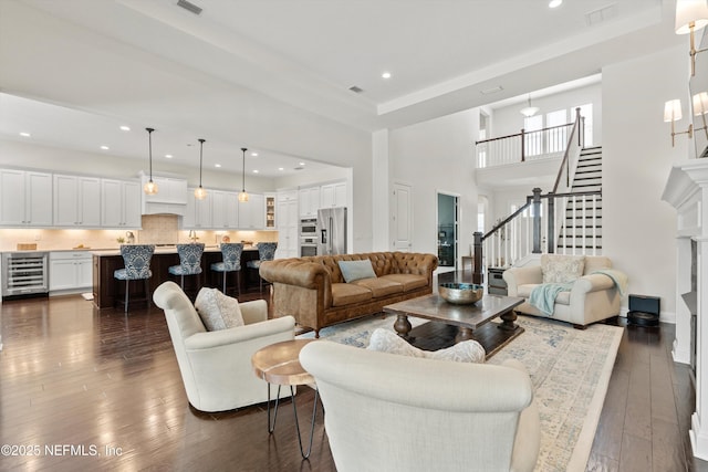 living room featuring a towering ceiling, visible vents, wine cooler, stairs, and dark wood-type flooring