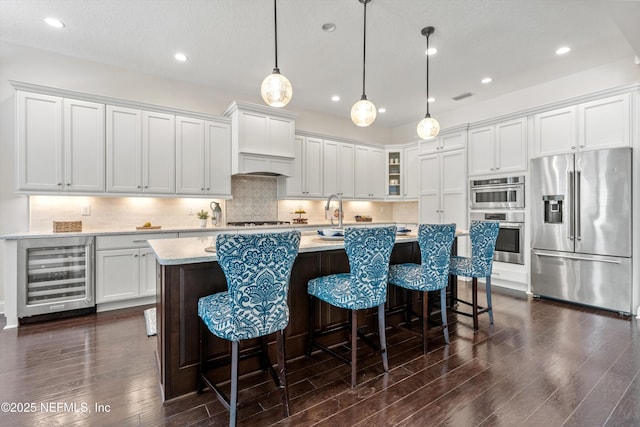 kitchen featuring light countertops, beverage cooler, stainless steel appliances, visible vents, and dark wood-style floors