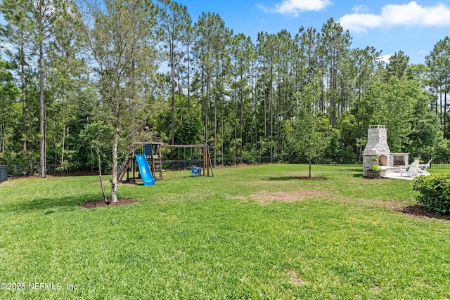 view of yard featuring an outdoor stone fireplace, fence, and a playground