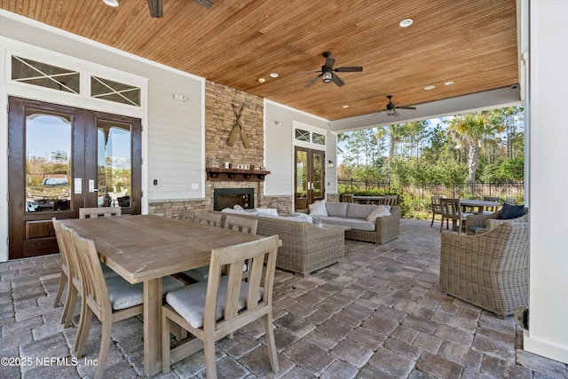 view of patio featuring fence, french doors, a ceiling fan, an outdoor living space with a fireplace, and outdoor dining space