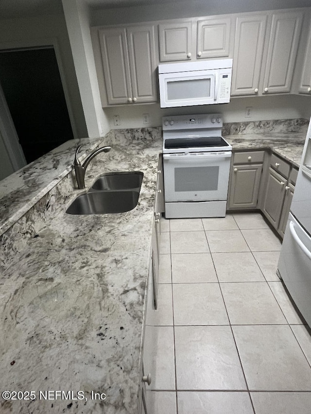 kitchen featuring white appliances, a sink, gray cabinets, light tile patterned floors, and light stone counters