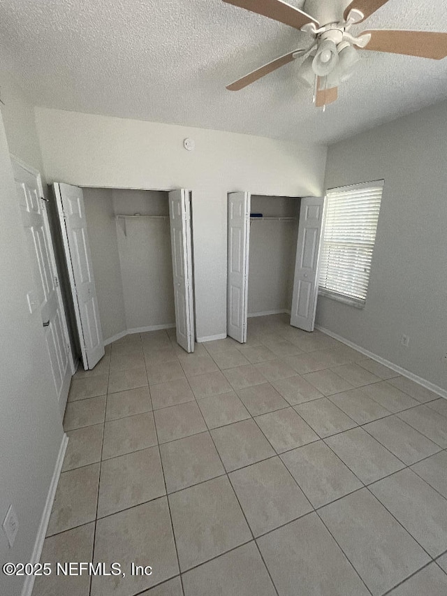 unfurnished bedroom featuring multiple closets, light tile patterned floors, a textured ceiling, ceiling fan, and baseboards