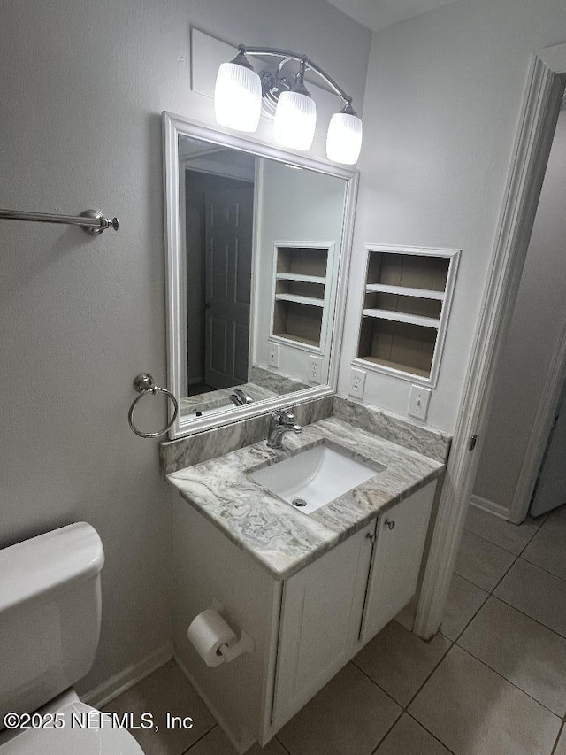 half bath with toilet, vanity, tile patterned flooring, and baseboards