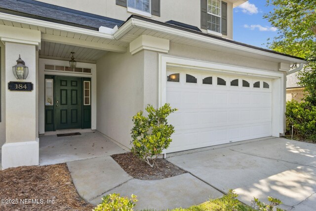 property entrance with concrete driveway, a garage, and stucco siding