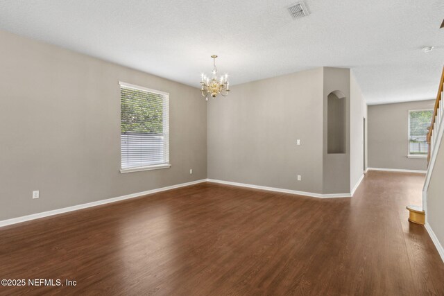 empty room featuring a chandelier, baseboards, visible vents, and dark wood finished floors