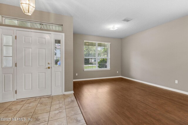 foyer featuring baseboards, a textured ceiling, light wood-style floors, and visible vents