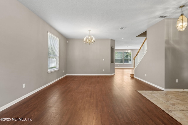 interior space featuring an inviting chandelier, stairs, baseboards, wood finished floors, and visible vents