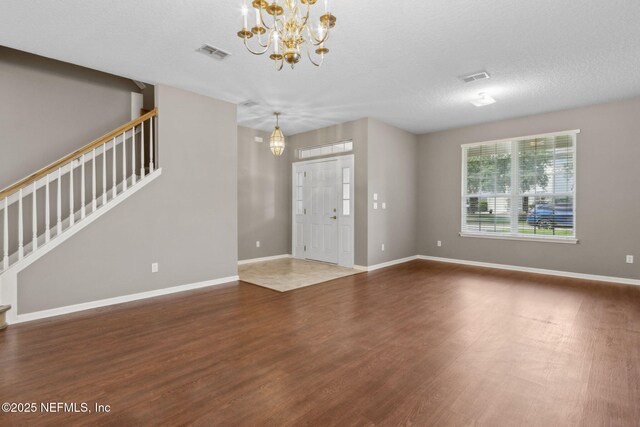 unfurnished living room with visible vents, stairs, wood finished floors, and an inviting chandelier