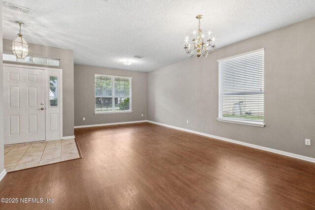 foyer with baseboards, a textured ceiling, wood finished floors, and a notable chandelier