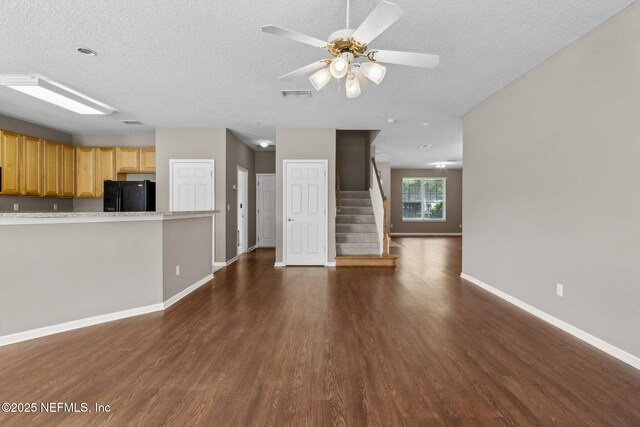 unfurnished living room featuring dark wood-style flooring, a textured ceiling, baseboards, visible vents, and stairway