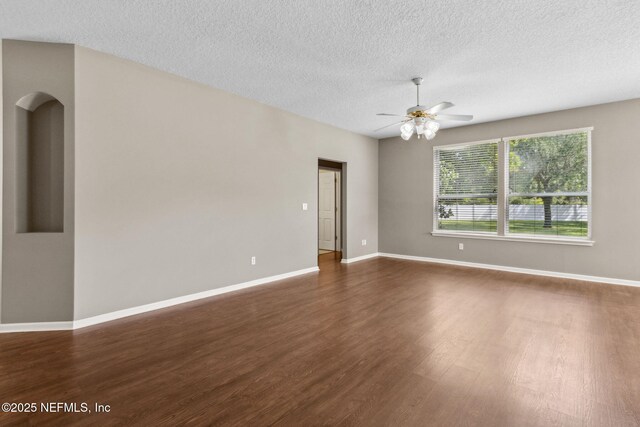 spare room with arched walkways, a textured ceiling, dark wood finished floors, a ceiling fan, and baseboards