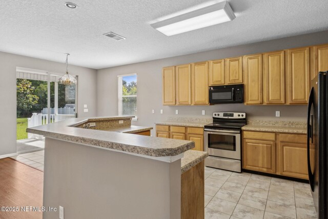 kitchen featuring light countertops, decorative light fixtures, visible vents, a center island with sink, and black appliances