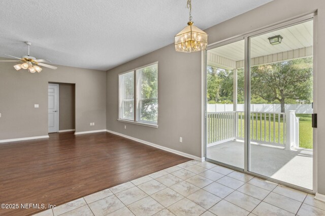 unfurnished dining area with baseboards, tile patterned flooring, ceiling fan with notable chandelier, and a textured ceiling