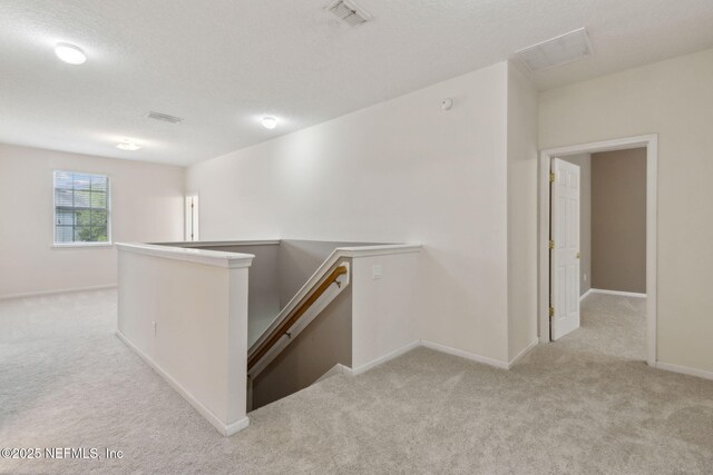 hallway with baseboards, an upstairs landing, light carpet, and visible vents