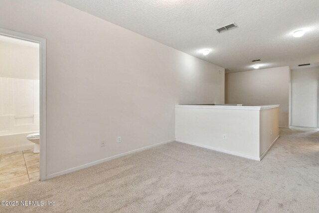 unfurnished room featuring baseboards, carpet, a textured ceiling, and visible vents