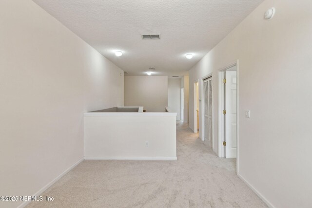 unfurnished room with a textured ceiling, visible vents, light carpet, and baseboards
