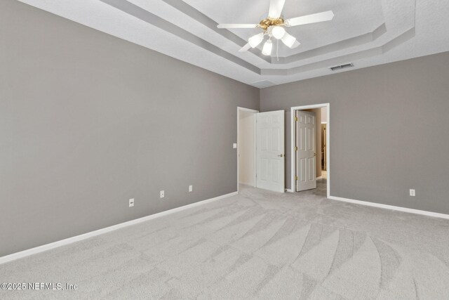 empty room featuring visible vents, baseboards, light colored carpet, a raised ceiling, and a ceiling fan