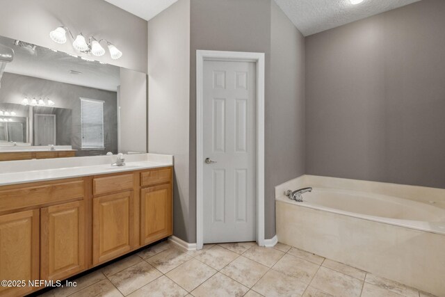 full bath with tile patterned flooring, vanity, a textured ceiling, baseboards, and a garden tub