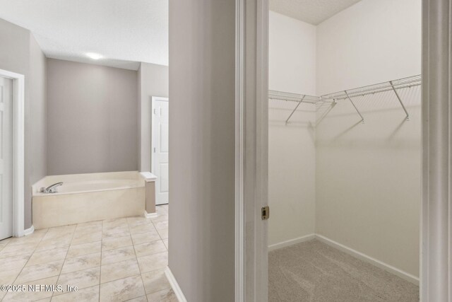 bathroom with a garden tub, baseboards, and a spacious closet