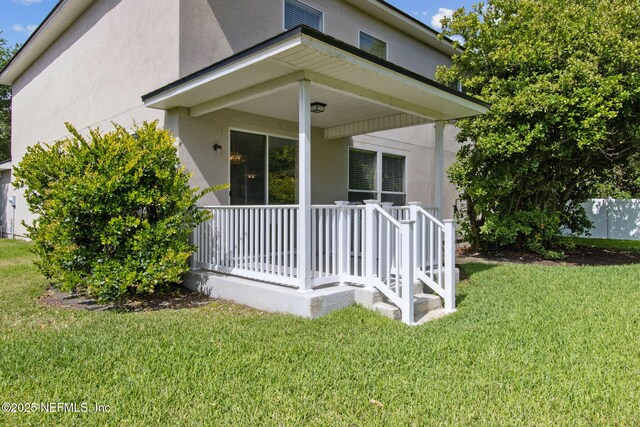 back of property with a lawn, covered porch, and stucco siding