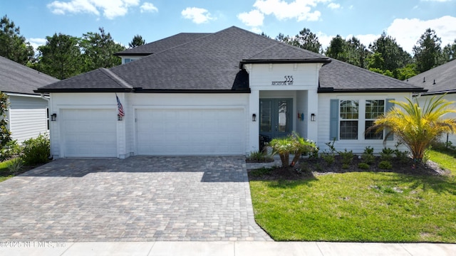 ranch-style home with french doors, a front yard, decorative driveway, an attached garage, and a shingled roof