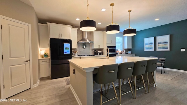 kitchen featuring light wood-style floors, freestanding refrigerator, backsplash, and wall chimney range hood