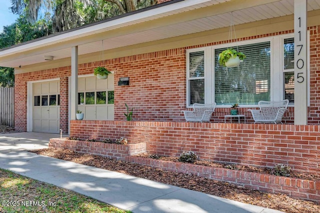 property entrance with a porch, an attached garage, driveway, and brick siding