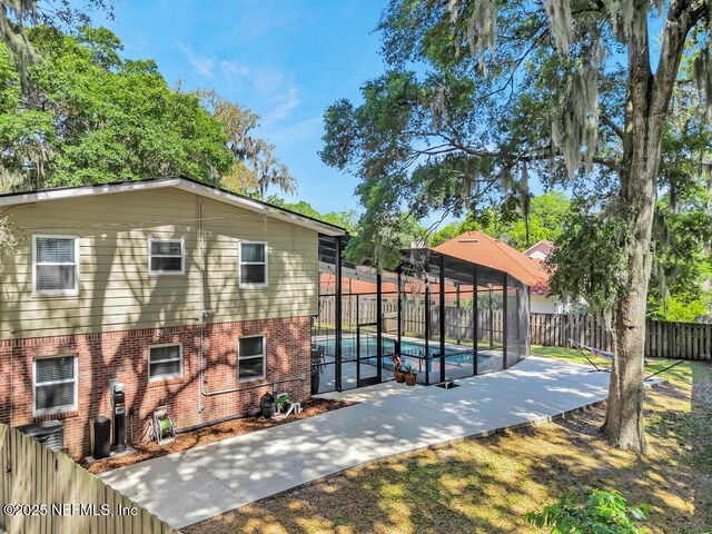 exterior space with brick siding, a fenced in pool, a fenced backyard, a patio, and glass enclosure