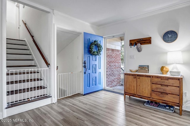 foyer with crown molding, stairs, and light wood-style flooring