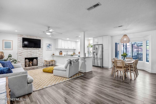 living area featuring visible vents, a fireplace, ceiling fan, a textured ceiling, and dark wood finished floors