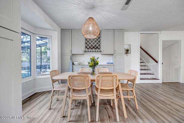dining area featuring baseboards, visible vents, stairway, and light wood-type flooring