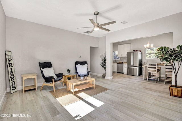 living area featuring baseboards, visible vents, light wood-style flooring, and ceiling fan with notable chandelier