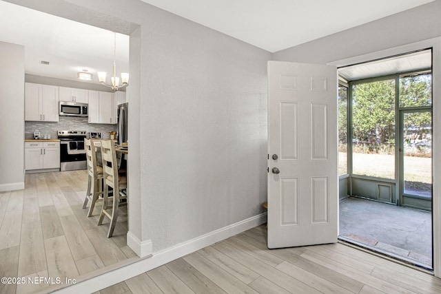 interior space featuring an inviting chandelier, baseboards, light wood-style floors, and visible vents