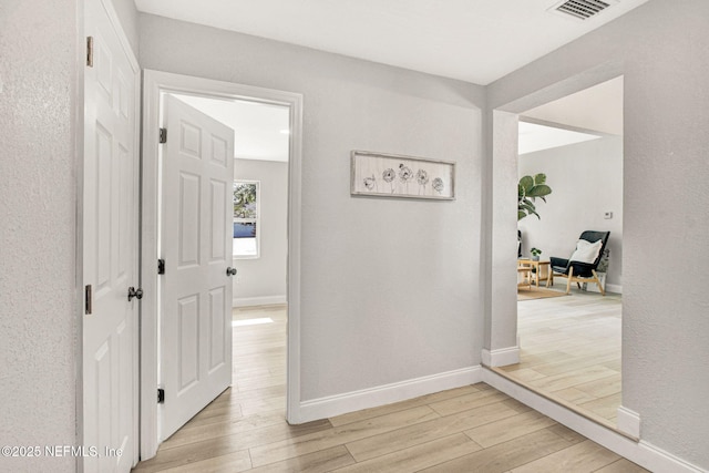 hall with visible vents, light wood finished floors, and baseboards