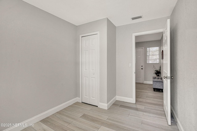unfurnished bedroom featuring visible vents, baseboards, a closet, and light wood-type flooring
