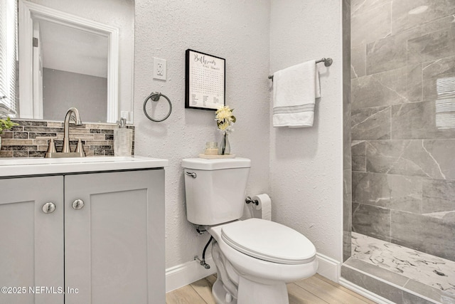 bathroom featuring toilet, tiled shower, wood finished floors, and vanity