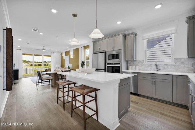 kitchen featuring gray cabinets, appliances with stainless steel finishes, a sink, open floor plan, and light wood-style flooring
