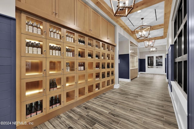 wine area with wood finished floors, baseboards, beam ceiling, and a chandelier